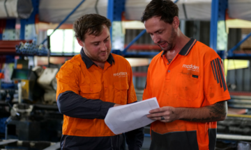 A photo of two men lookuing at a piece of paper in a warehouse